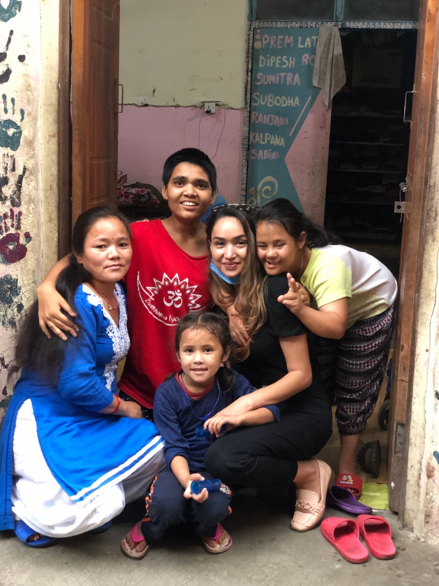Pooja crouched in a doorway at Bal Mandir with a young girl and three women