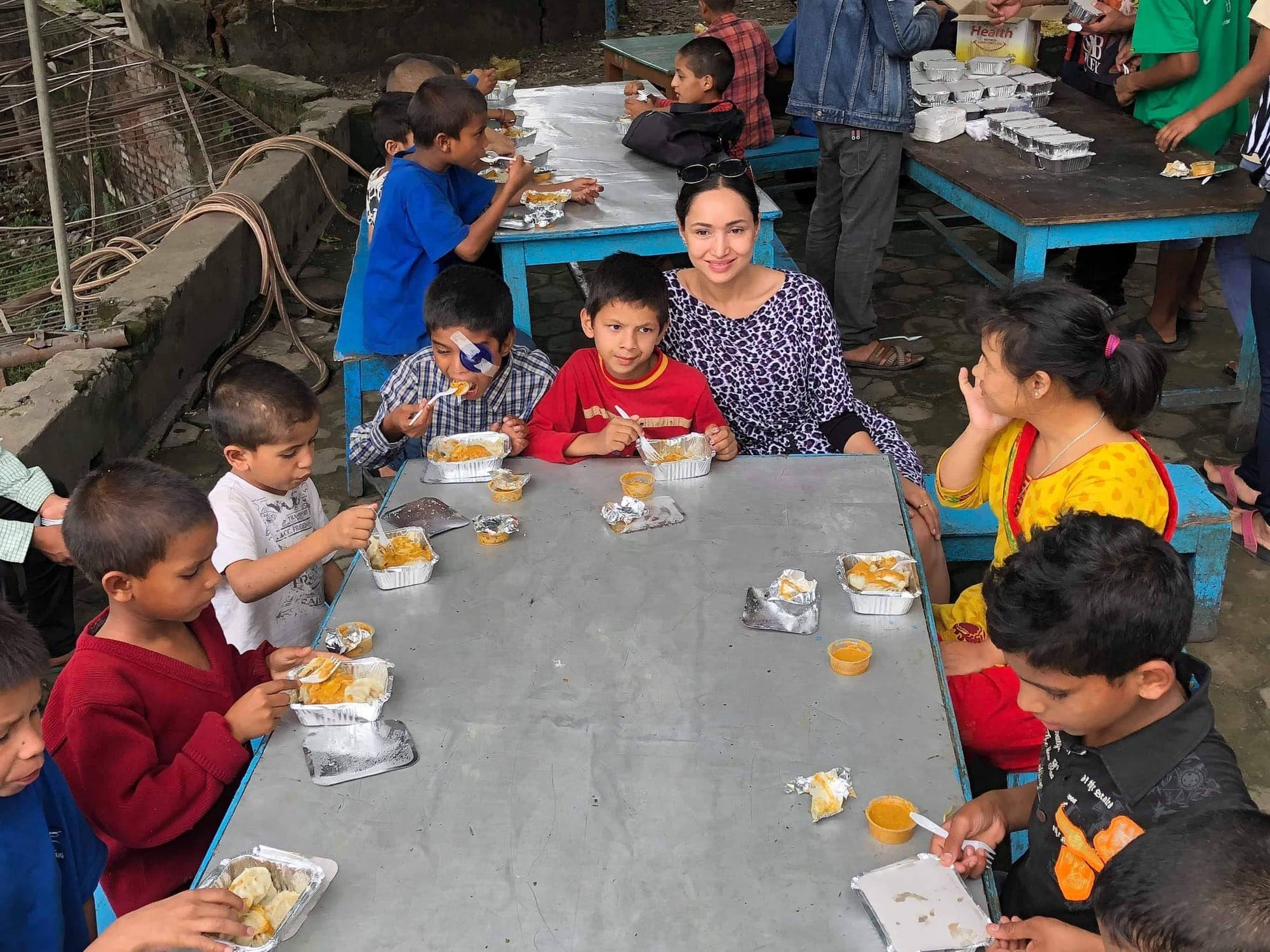 Pooja sitting with children over lunch at an outdoor table at Bal Mandir