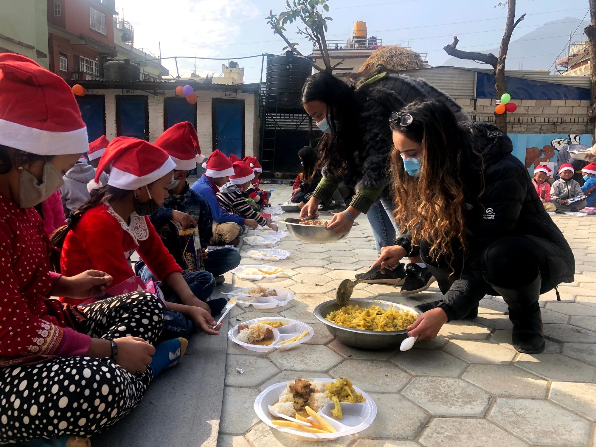 Pooja and a volunteer serving a festive lunch onto plates in the courtyard