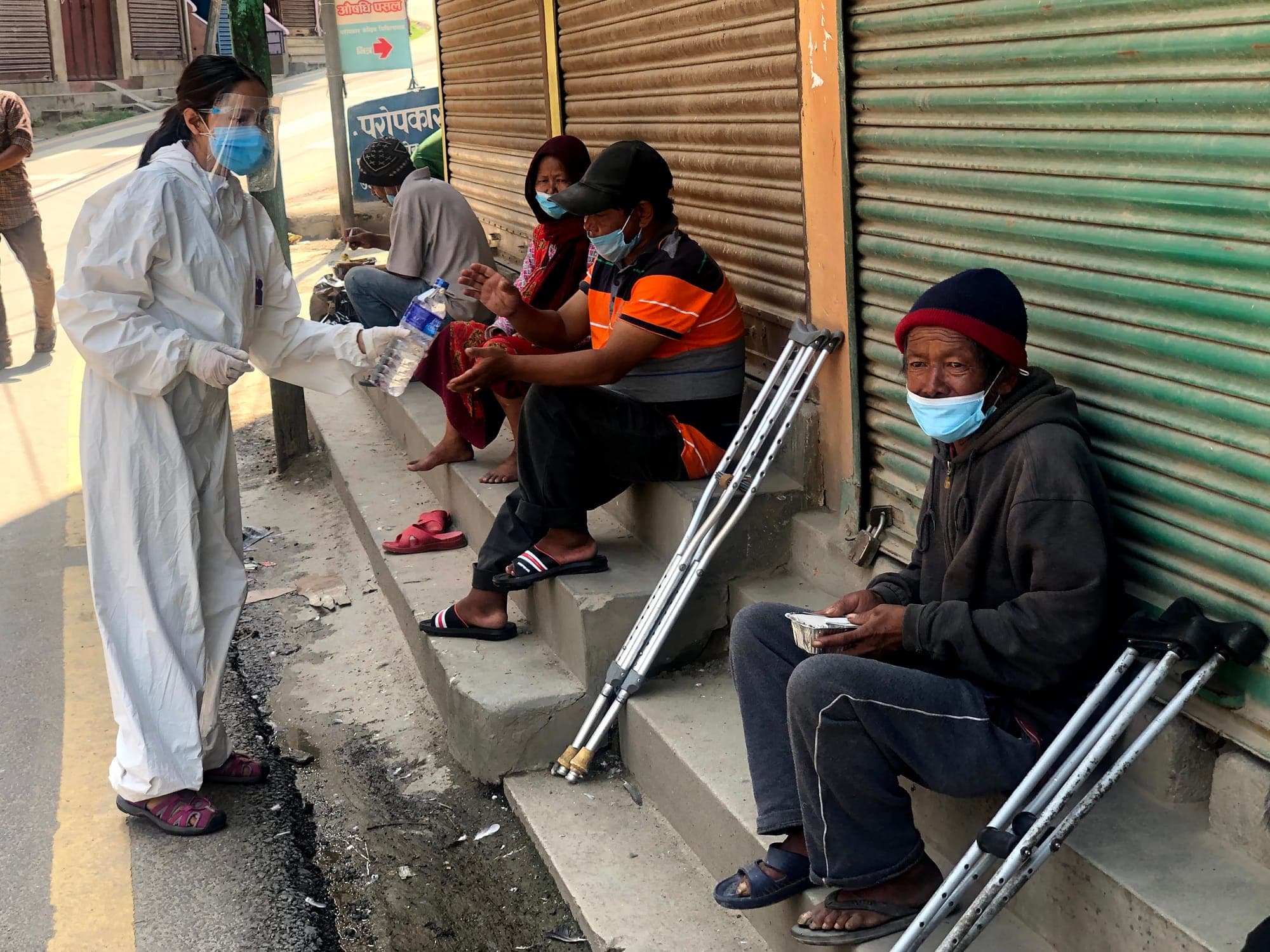Men resting on shopfront steps, their crutches beside them, being handed water and a meal during the 2020 lockdown