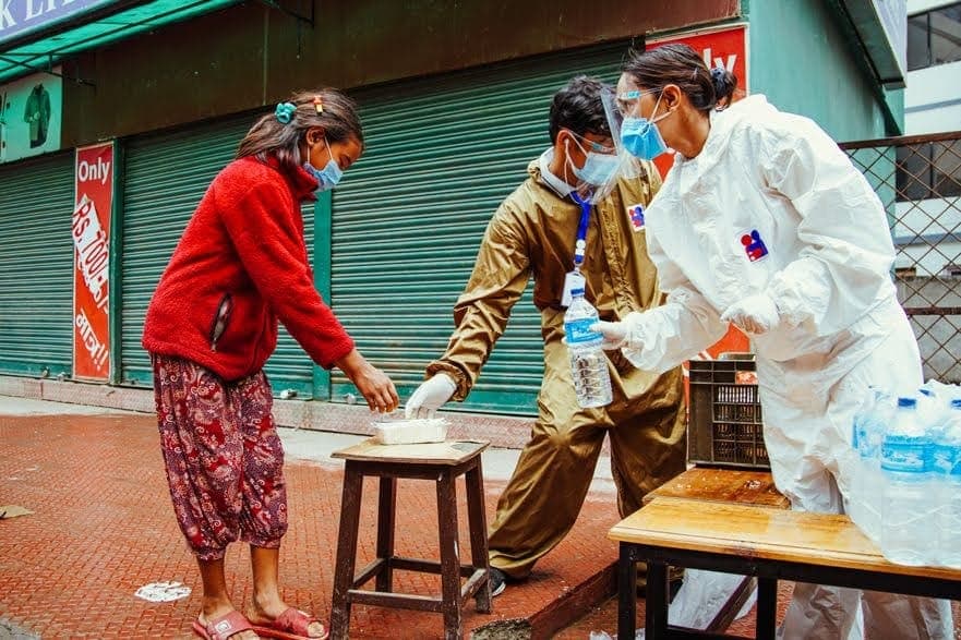 A woman collecting a meal from a stool set out on the pavement