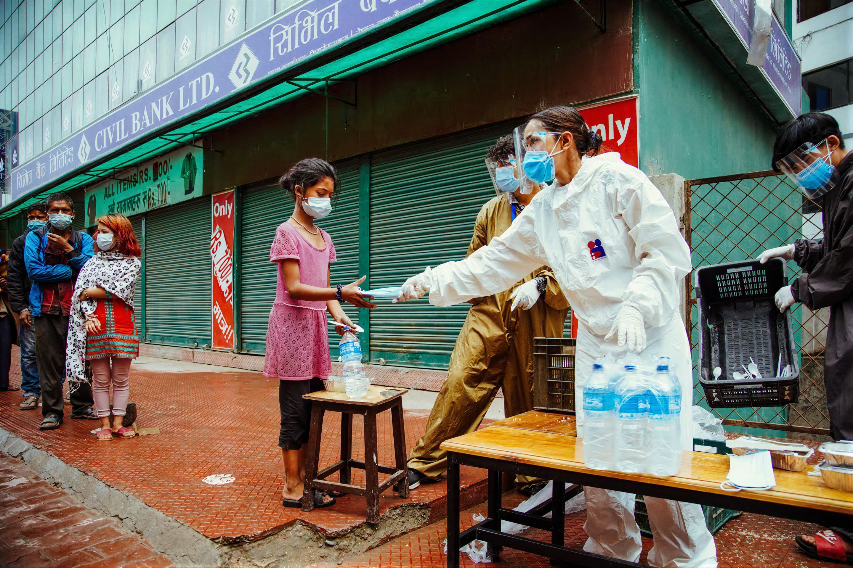 Pooja, in protective gear, handing out food and water on a Kathmandu street during the 2020 COVID-19 lockdown