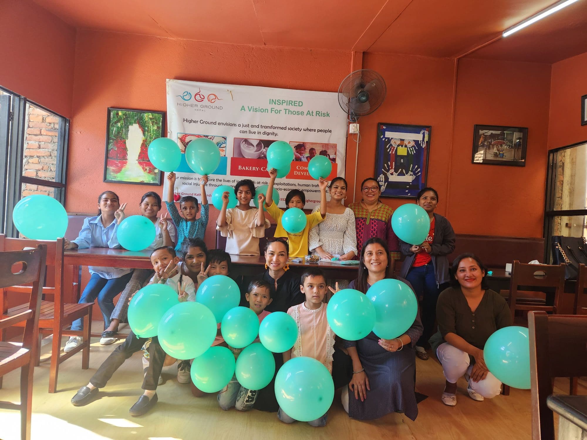 Pooja with Higher Ground staff and children holding up balloons beneath the Higher Ground banner