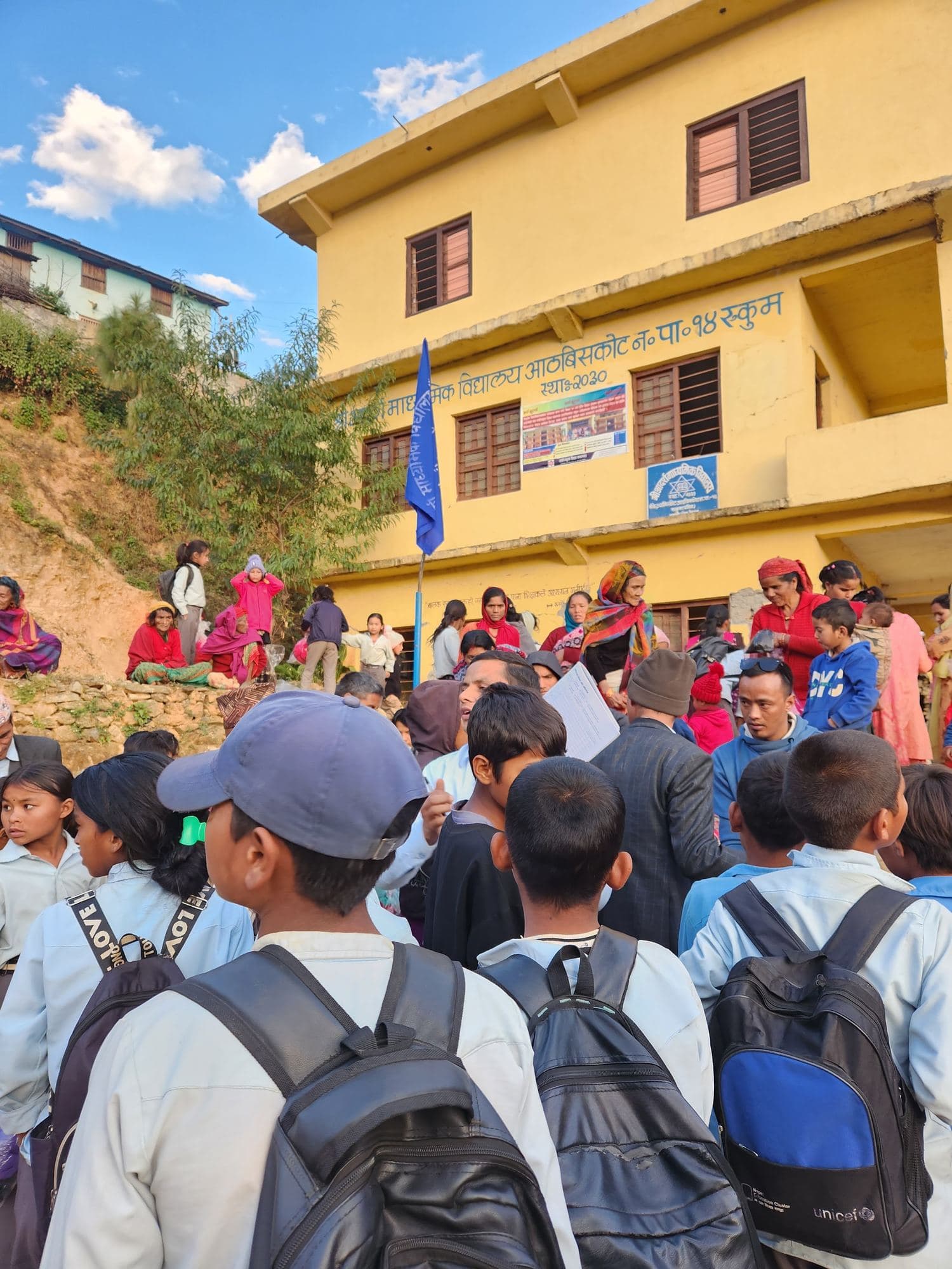 Students, seen from behind, gathered in front of the school