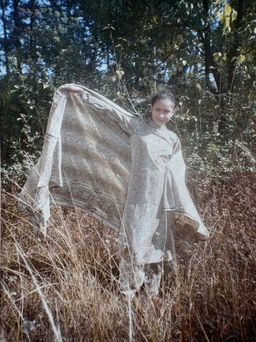 Pooja as a girl, holding a shawl open like wings in tall grass