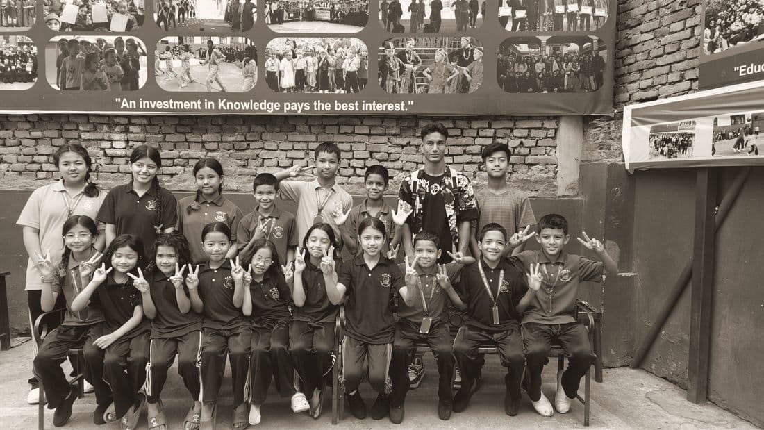 Students in uniform sitting together on a bench, waving