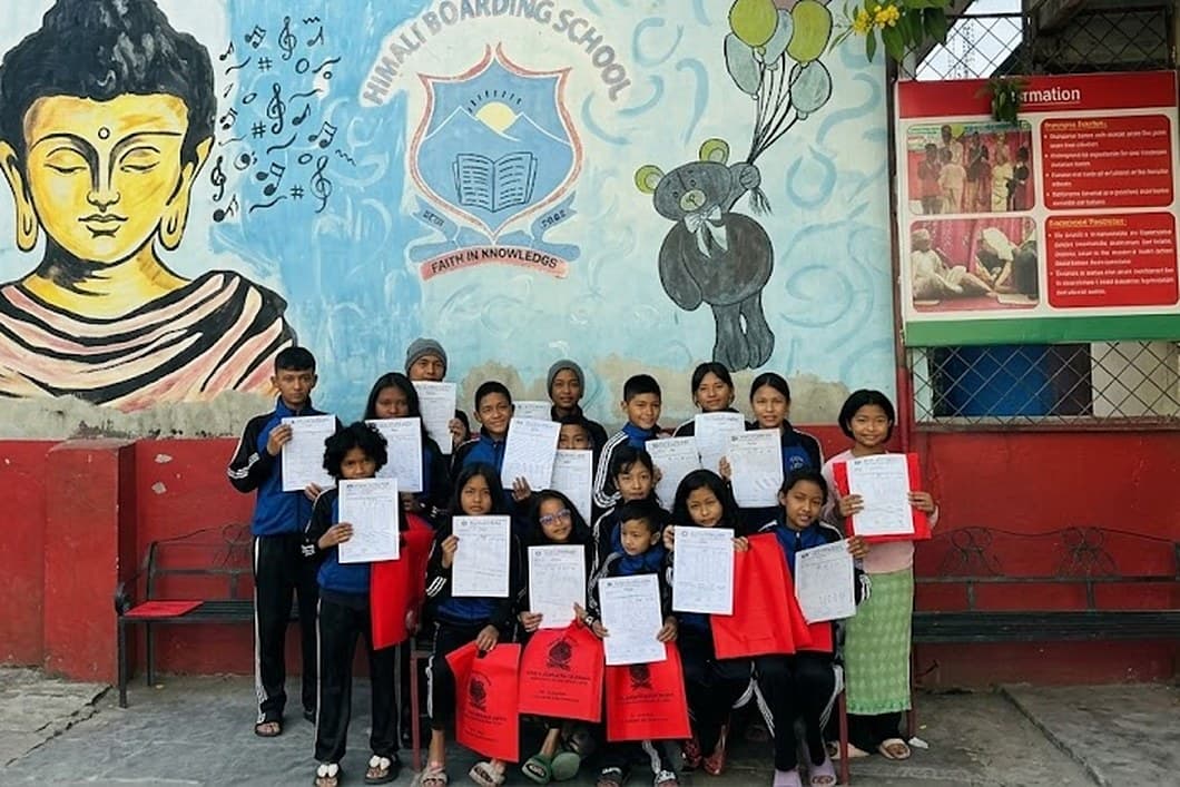 Children holding up their work in front of a painted school wall