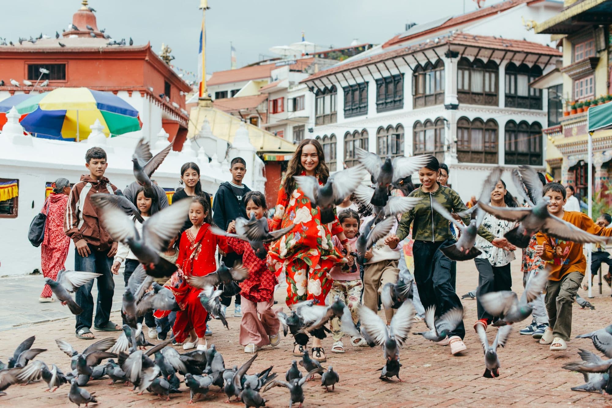 Pooja running with the children across the square at Boudhanath, pigeons taking off around them