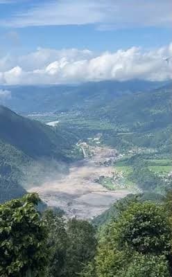 Grey floodwater filling the valley floor below green hills