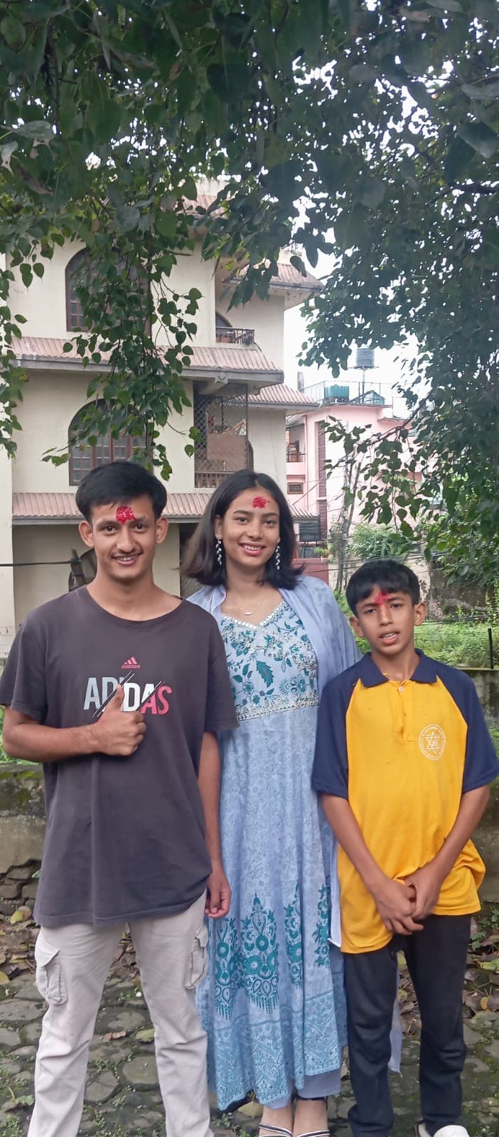Uma at Dashain with tika on her forehead, standing outside between her two brothers