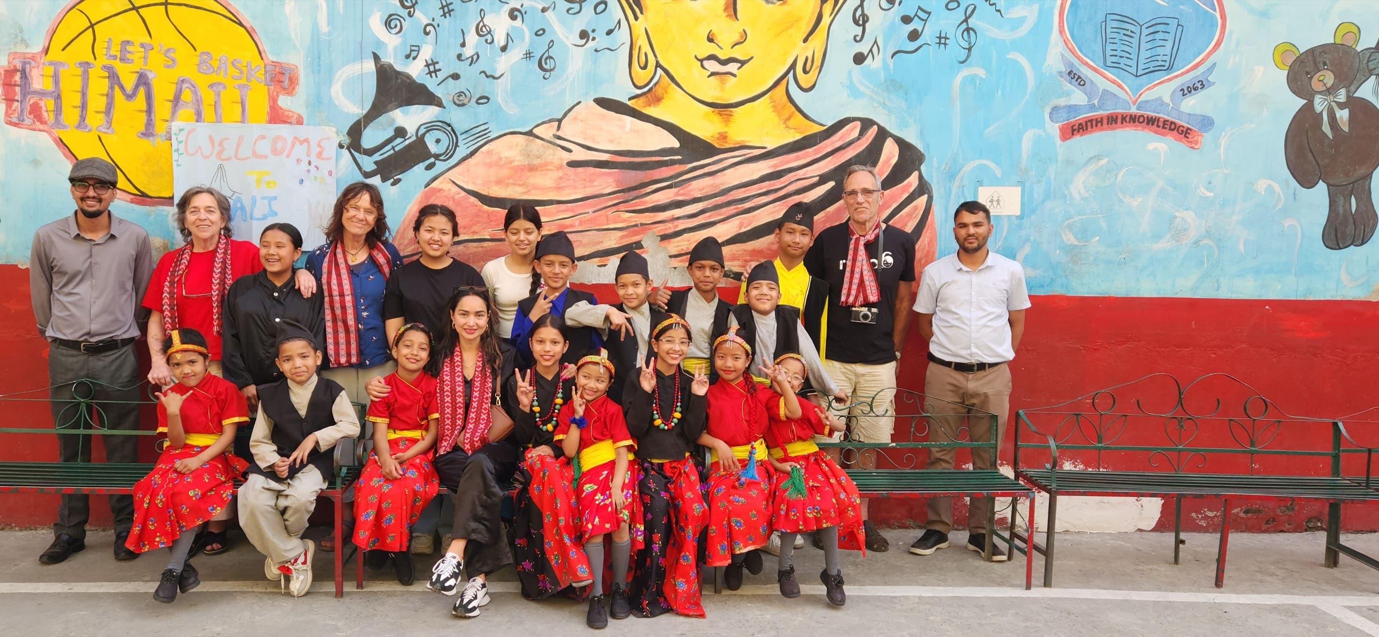 The Ruta6 team and Pooja with children in traditional dress, in front of a painted mural at Himali Boarding School