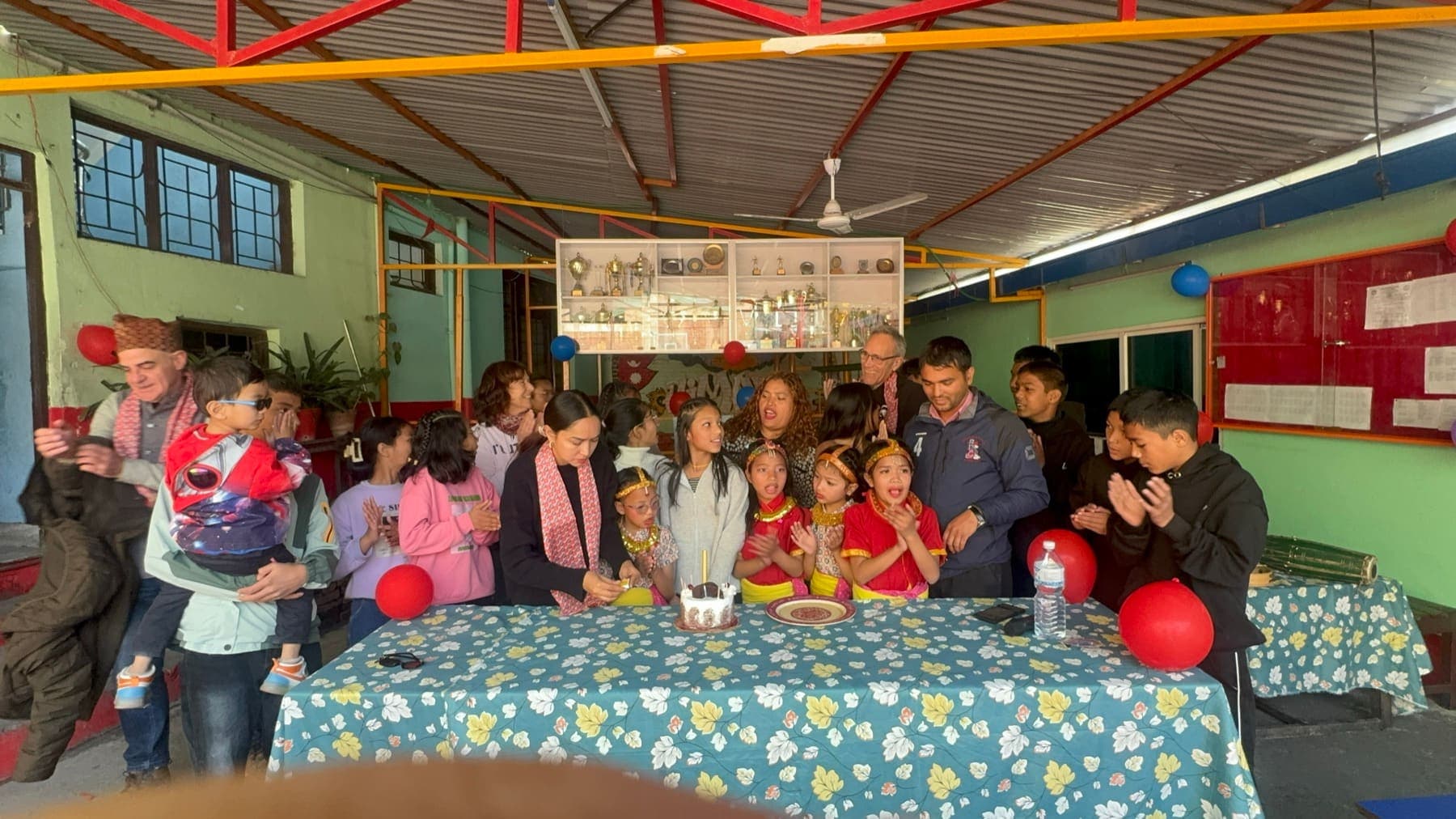 The Ruta6 team, Pooja and the children clapping around a birthday cake under a school canopy