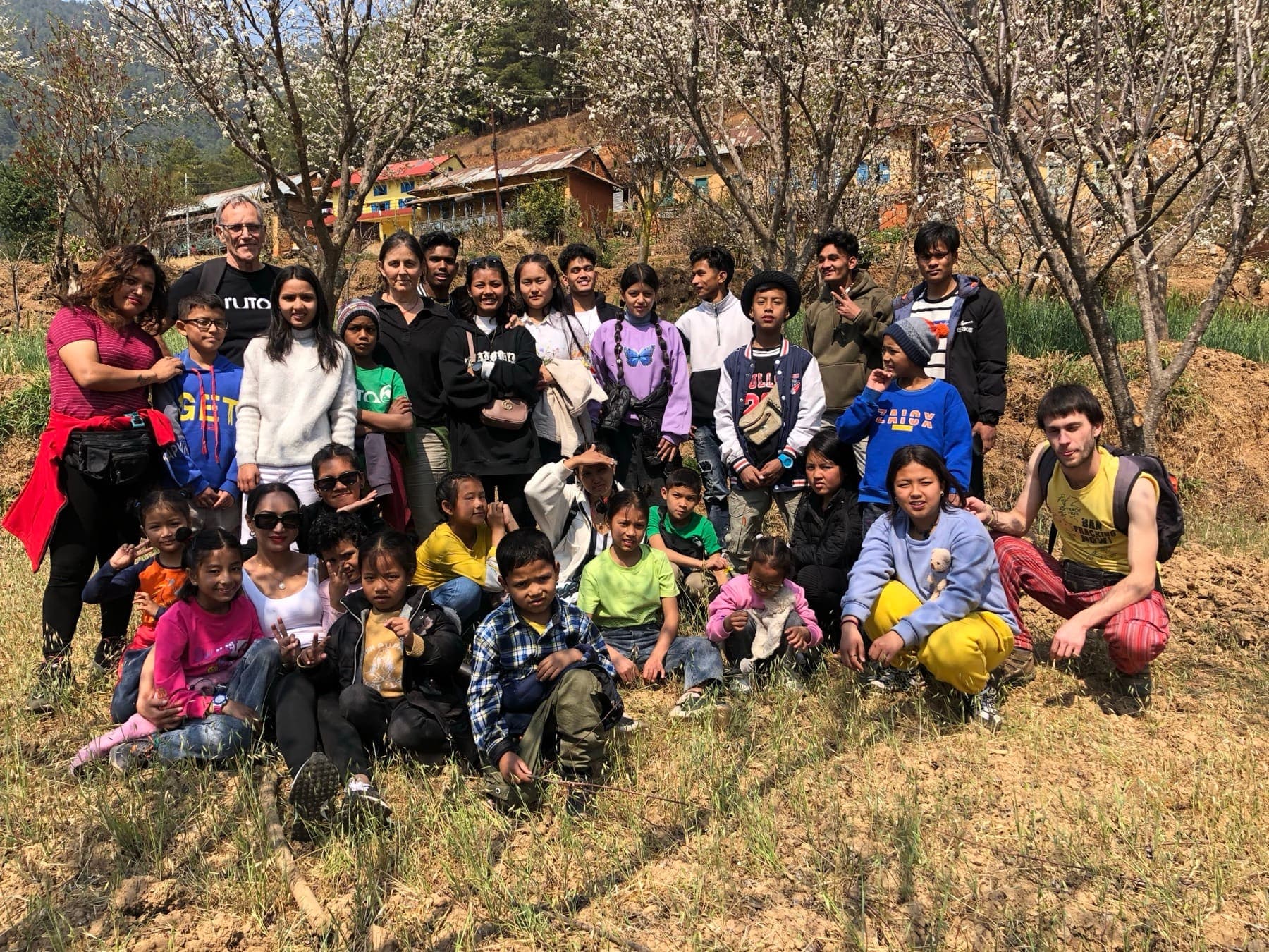The Ruta6 team, Pooja and the children in a field under blossoming trees, with a village behind